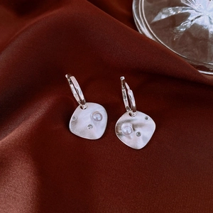 Macro detail of silver geometric pearl earrings with zircon on red silk background