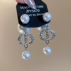 Close-up of pearl earrings featuring pavé crystals and iconic silver CD letter charms