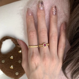 18 Karat vergoldeter ovaler roter Zirkonring am Finger vor weichem rosa Stoffhintergrund
