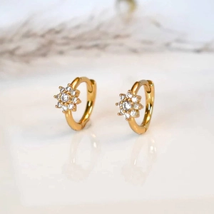 Macro detail of gold flower hoop earrings with zircon crystals on a white mirror