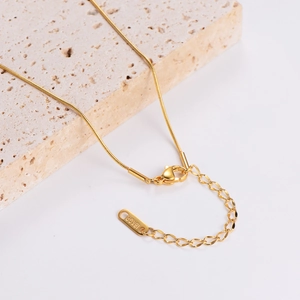 18KGP gold plated snake chain necklace with lobster clasp on a beige travertine stone