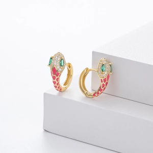 Macro detail of gold snake earrings with pink enamel scales and green gemstones