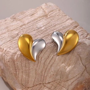 Two-tone gold and silver heart earrings with polished finish on a stone surface