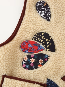 Detail of beige sherpa fleece vest with heart-shaped embroidered patches and brown piping