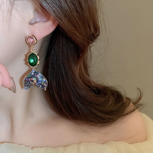 Close-up of dangling mermaid tail earrings with pink and green stones on a model