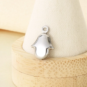 Detailed close-up of a silver stainless steel Hamsa Hand pendant on a beige fabric ring stand