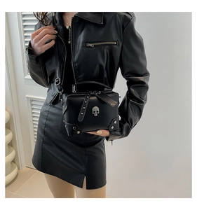 Detail of black matte leather crossbody bag with silver skull ornament and metal rivets