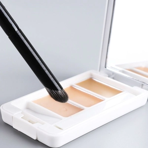 Vue macro d'un pinceau correcteur de précision prélevant de la crème d'une palette