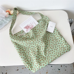 Flat lay of a green floral canvas tote bag with books and tulips on a white desk