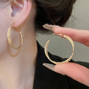 Detail view of gold layered geometric twisted hoop earrings worn and held for scale
