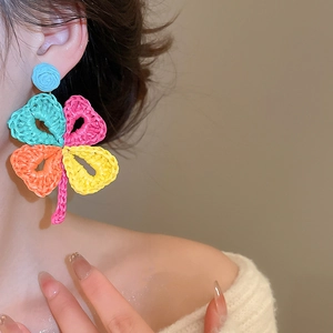 Detailed shot of handmade woven raffia four-leaf clover earrings on model's ear
