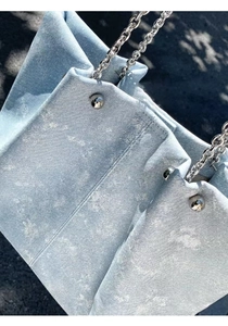 Close-up of light blue denim tote bag with silver chain strap and metal buckle detail