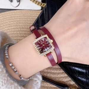 Close-up of women's gold square watch with red dial and double wrap leather strap