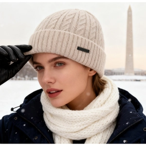 Winter cable knit beanie in beige with leather label shown in a snowy outdoor setting