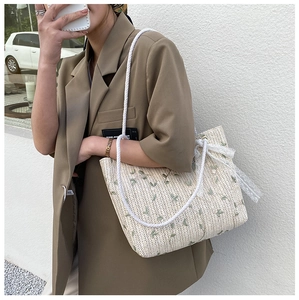 Detailed embroidery of green flowers and lace bow on a beige woven straw tote bag