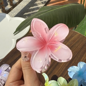 Pink plumeria hair claw clip with jelly texture held against a wooden background