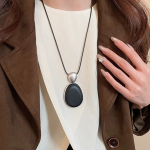 Détail du pendentif goutte argentée et bois noir ovale sur un long collier minimaliste