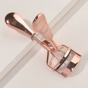 Rose gold stainless steel eyelash curler with black rubber pad on minimalist background