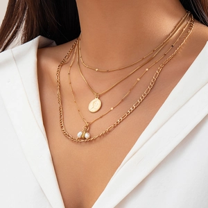 Detail of layered gold necklaces with coin and pearl pendants on a female model
