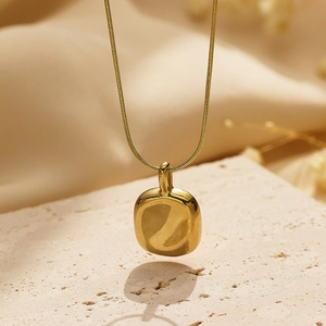 Detailed view of a gold snake chain necklace with an organic square pendant on stone