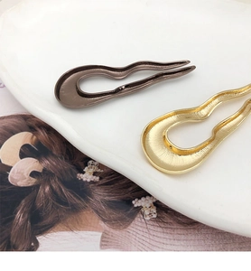 Macro detail of brown and gold U-shaped metal hairpins with wavy design on a white plate