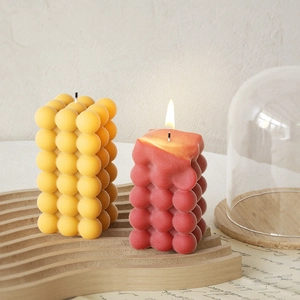 Dettaglio di candele a cubo con bolle gialle e arancioni su vassoio in legno