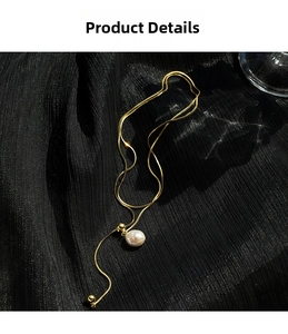 Close-up of golden snake chain with a glossy white baroque pearl on black fabric
