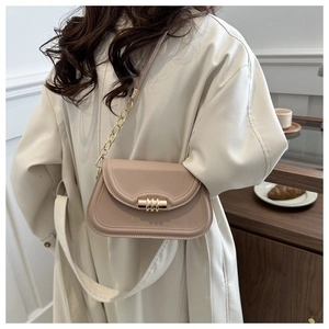 Detail of beige saddle bag with gold cylinder lock and chain strap on a model