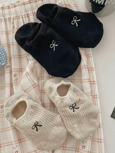 Detail of rib knit socks featuring embroidered bows in black and beige colors