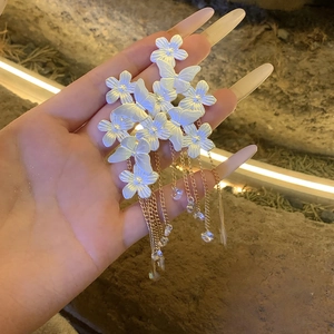 Close-up of white crystal butterfly flower earrings with elegant long gold tassel chains
