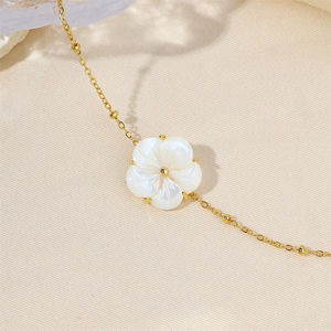 Detail of a 18k gold plated bracelet featuring a white shell flower and small gold beads