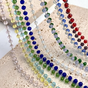 Macro view of multi-colored faceted crystal bead necklaces on a beige stone surface