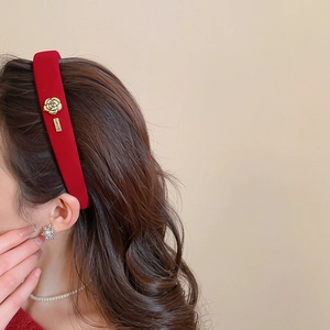 Gros plan d'un serre-tête en velours rouge avec rose dorée et petite plaque de marque