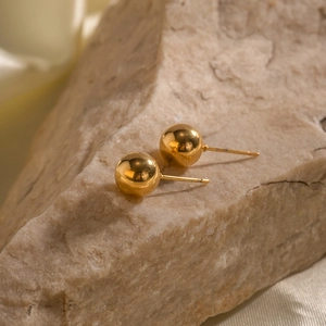 Minimalist golden ball stud earrings displayed on natural stone with silk fabric