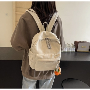 Detail of light white corduroy backpack with carrot charm worn by a model in a room