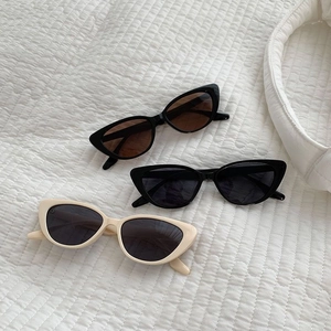 Three retro cat-eye sunglasses in black and beige colors on a white quilted surface
