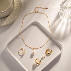 Elegant gold pearl jewelry set with necklace, ring and earrings on a white ceramic plate
