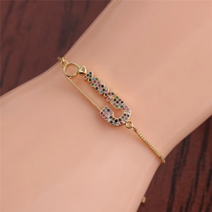 Detailaufnahme des goldenen Sicherheitsnadel-Armbands mit bunten Zirkoniasteinen am Handgelenk