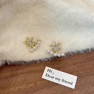 Detail of 18k gold plated snowflake earrings featuring zircon and hanging pearls