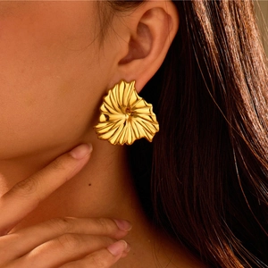 Close-up of a large gold fan-shaped metal earring with textured pleats on a model