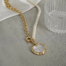 Detailed macro of gold-plated bow necklace with pearl chain and heart shell pendant