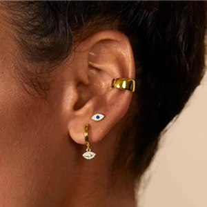 Close-up of gold cartilage piercing set with blue evil eye stud and smooth ear cuff