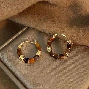 Detail of gold hoop earrings with amber resin beads on a brown velvet surface