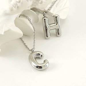 Macro detail of puffy silver bubble initial letters C and H on polished necklaces