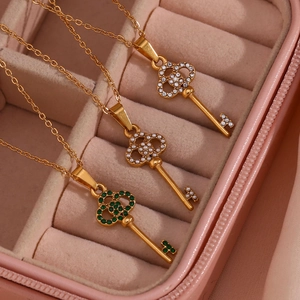 Close-up of golden key necklaces with crystals and emerald on pink velvet
