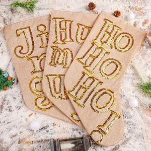 Three beige linen Christmas stockings with gold sequin letters on white snow background