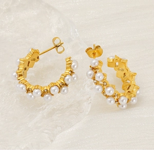 Detail of golden C-shape earrings with pearls and rhinestones on a textured background