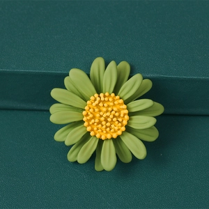 Macro detail of a matte green daisy brooch with a yellow core on a dark textured base