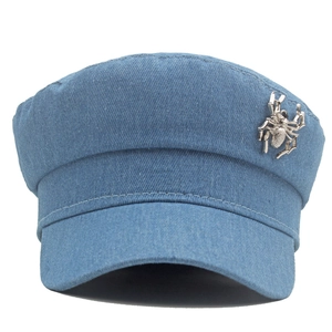 Détail de la casquette en denim bleu avec une broche en métal argenté en araignée