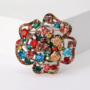Detail of a 3D gold flower brooch featuring colorful rhinestones on a white pedestal